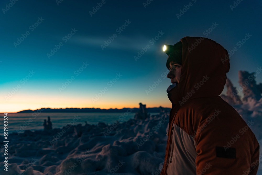 Teenager boy in a warm winter jacket with a headlamp on a mountain winter trail. Minutes before sunset, Babia Gora, Beskids, Poland