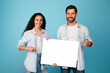 © Prostock-studio - Happy young middle eastern wife and european bearded husband show finger on banner with blank space