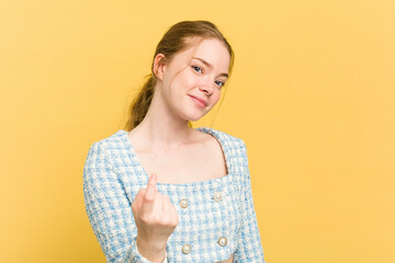 Wall Mural - Young caucasian redhead woman isolated on yellow background pointing with finger at you as if inviting come closer.