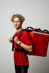 Canvas Print - Side view of young courier in a red uniform and with a thermo bag on color red background, space for text. Fast express home delivery. Online order.