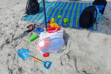 Children's Beach Toys, Sandals And Knapsacks On Beach Sand Near A Multi-colored Beach Blanket