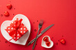 Saint Valentine's Day concept. Top view photo of heart shaped dish with present box cutlery chocolate candies and confetti on isolated red background with copyspace