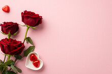Valentine's Day Concept. Top View Photo Of Bouquet Of Red Roses And Heart Shaped Saucer With Chocolate Candies On Isolated Pastel Pink Background With Copyspace