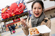 © PR Image Factory - happy Asian Japanese girl looking at camera and showing takoyaki in box with a big octopus sign at background food district in Shinsekai area in Osaka Japan