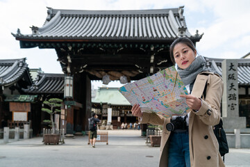 Wall Mural - portrait of Asian Japanese female tourist holding and looking at a map at the entrance of Osaka Tenmangu Shrine in japan. translation: âOsaka Tenmangu Shrineâ