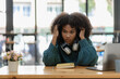 © ArLawKa - African american girl writing in notebook sitting at desk with laptop. Working hard. Woman wearing headphones while working online. Student excited to learn language online in cafe.
