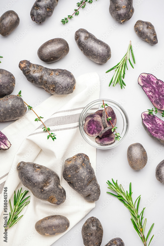 Composition with cut and whole purple potatoes and herbs on white background