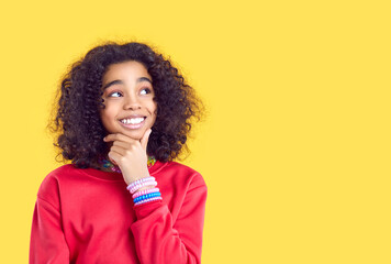 pensive smiling african american girl isolated on yellow studio background look at copy space aside.