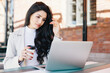 © VK Studio - European female freelancer thinking on ideas for her new project working with laptop computer while sitting at outdoor cafeteria and drinking takeaway coffee having serious and thoughtful expression