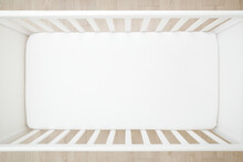 Empty Baby Crib With White Mattress On Wooden Home Floor. Closeup. Top Down View.