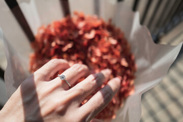 Wall Mural - Close up of diamond ring on woman’s finger while touching orange flower with sunlight and shadow. Love, valentine, relationship and wedding concept. Soft and selective focus.