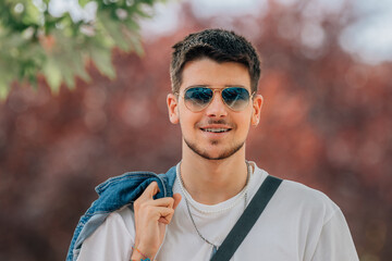 Wall Mural - portrait young man walking with mobile phone and sunglasses in summer