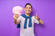 © Bangun Stock Photo - Smiling young Asian man wearing white t-shirt pointing fingers at cash money in rupiah banknotes isolated over purple background. people lifestyle concept