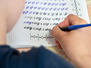 Writing homework. Close-up of girl hand with pen writing russian words by hand on traditional white notepad paper. The girl writes his first letter in Russian.