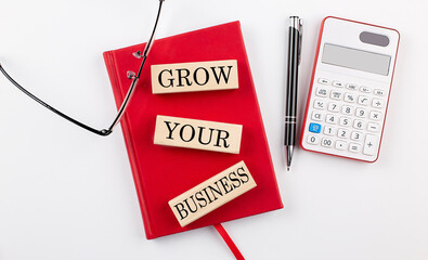 Poster - GROW YOUR BUSINESS text on wooden block on red notebook