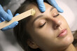 Young woman undergoing hair removal procedure on face with sugaring paste in salon, closeup