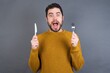 © Jihan - Young handsome caucasian man wearing yellow knitted sweater over gray background holding a fork and knife feeling excited looking front