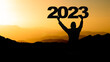 Happy new Year - Landscape background banner panorama 2023 - Breathtaking view with black silhouette of mountains and man holding year, in the morning during the sunrise