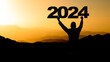Happy new Year - Landscape background banner panorama 2024 - Breathtaking view with black silhouette of mountains and man holding year, in the morning during the sunrise