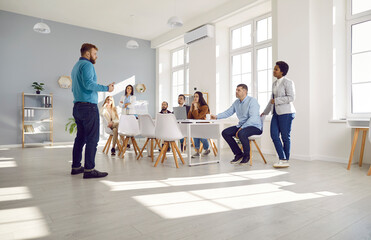 Young man who is a corporate manager talking to a multiracial business team. Mixed race multiethnic group of people having a work meeting in a spacious light modern office with big windows