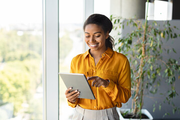 Aufkleber - Happy black female entrepreneur using tablet standing near window at modern coworking office, copy space