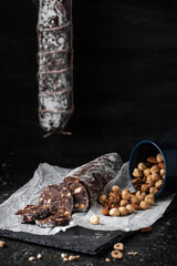 Canvas Print - Chocolate salami filled with almonds, hazelnuts and raisins on the black background. Italian sweet sausage shaped dessert sprinkled with powdered sugar. Christmas and New Year festive pastry