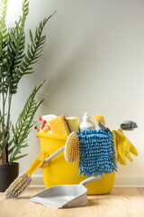 Brushes, bottles with cleaning liquids, sponges, rag and yellow rubber gloves on white background. Cleaning supplies in the yellow bucket on the wooden floor. Cleaning company service advertisement