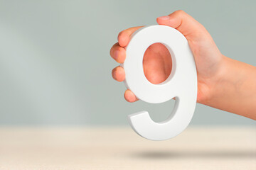Fototapete - Number nine in hand. A hand holds a white number 9 on a blurred background. Concept with number nine. Birthday 9 years, percentage, ninth grade or day.