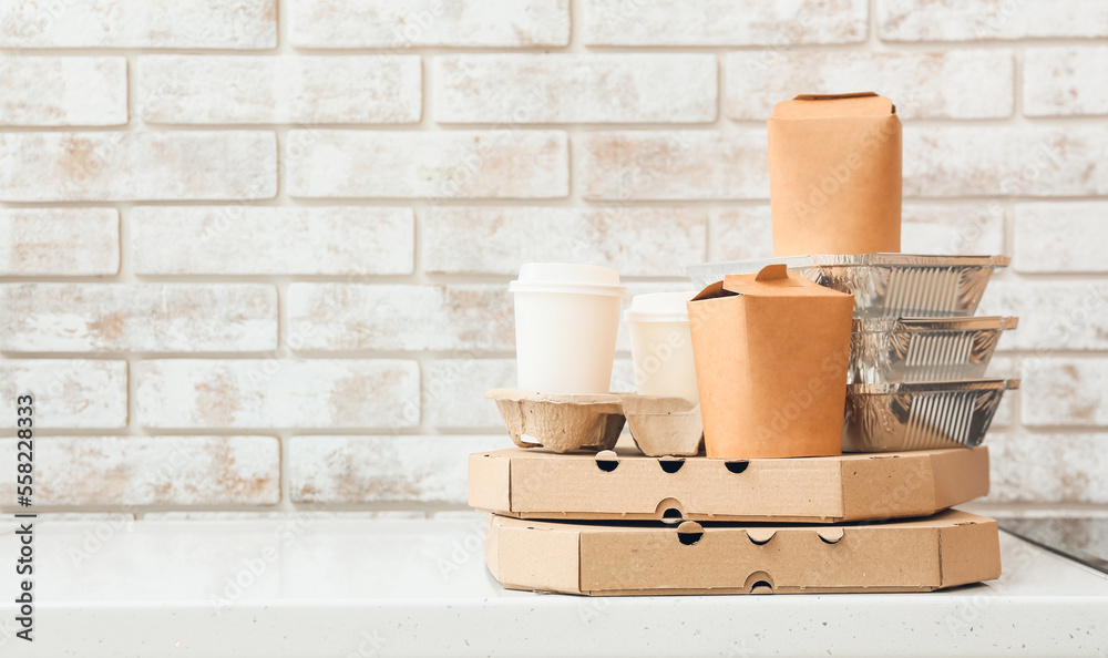 Set of different food delivery containers on white table near light brick wall