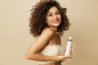Leinwanddruck Bild - Woman applies cream and balm to her curly hair, the concept of protection and care with salon products, a healthy look, a smile with teeth on a beige background