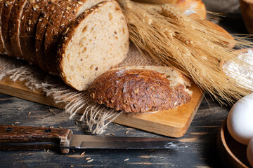 Wall Mural - Wheat flour, sliced bread  with sesame seeds, wheat ears and straw on an old wooden background