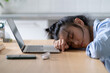 Tired Asian student girl lying on table in front of laptop, sleeping, taking break during online learning. Female freelancer napping at home office, feeling lazy to work remotely. Selective focus