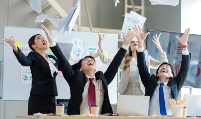 Wall Mural - Millennial Asian young professional successful male female businessmen businesswomen in formal suit laughing smiling throwing paperwork documents up in air celebrating together in company office