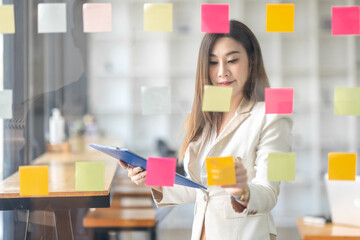 Wall Mural - Business female employee with many conflicting priorities arranging sticky notes commenting and brainstorming on work priorities colleague in a modern office.
