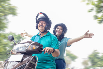 Happy senior indian couple wearing helmet riding motor scooter on road. Retirement life, Adventure and travel, Closeup