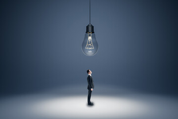 Aufkleber - Innovation, solution and creativity concept with businessman in black suit looking up at the ceiling with a big hanging light bulb on abstract empty grey area background