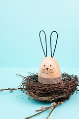 Wall Mural - Easter bunny or rabbit sitting in a bird nest, willow branches, wooden egg, spring holiday, brown and blue color