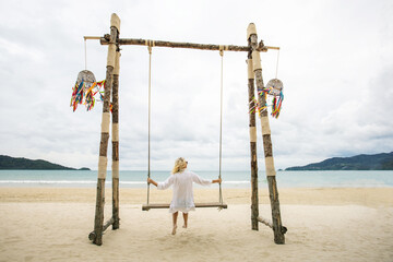 Wall Mural - Caucasian woman tourist relax and fun with swing on tropical sand beach. Travel on holidays or vacations to tropical country.