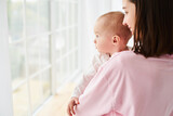 Fototapeta  - A small child, a boy, a baby in his mother's arms looks out the window.