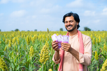 Happy farmer couting money or currency at agricultural farmland - concept of profit or earnings, banking or financial and agri business