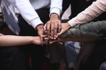 View of diverse senior and young people sitting in circle and putting hands together in community meeting or group therapy session. Concept of support, unity, success, help and trust.