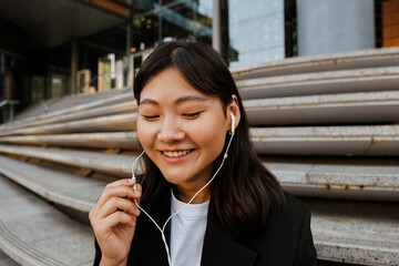 Wall Mural - Young asian woman in earphones smiling and listening music outdoors