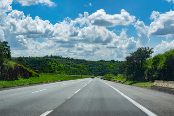 Wall Mural - cars on the road in the countryside surrounded by trees and a beautiful cloudy and blue sky