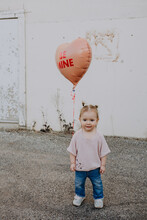 Happy Toddler Standing Outside With Heart Valentines Day Balloon