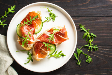 Sticker - Open sandwiches with cream cheese, prosciutto, cucumber and arugula at wooden table.