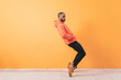 ©  Yistocking - Dark-skinned man dancing to favorite song standing on tiptoes with hands in pockets isolated over orange background wall, pointing at copyspace. Men doing disco moves enjoying sound and music, banners