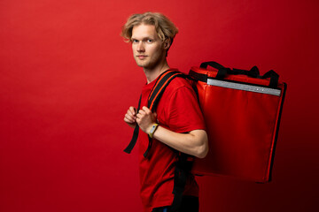 Sticker - Portrait of young courier with curly hair in red uniform with red thermo bag on red background looks straight in camera. Food delivery service.