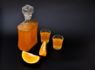 Orange liqueur, strong homemade alcohol with pieces of ripe citrus on a black background.