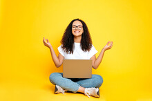 Full-length Photo Of A Positive Lovely Latino Or Brazilian Woman, In Casual Wear, Sitting With An Open Laptop In A Lotus Position With Eyes Closed On Isolated Yellow Background, Relaxing, Meditating
