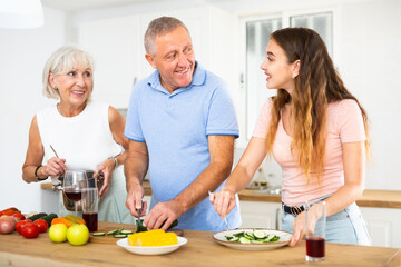 Wall Mural - Happy smiling parents enjoy weekend cook with adult daughter in kitchen